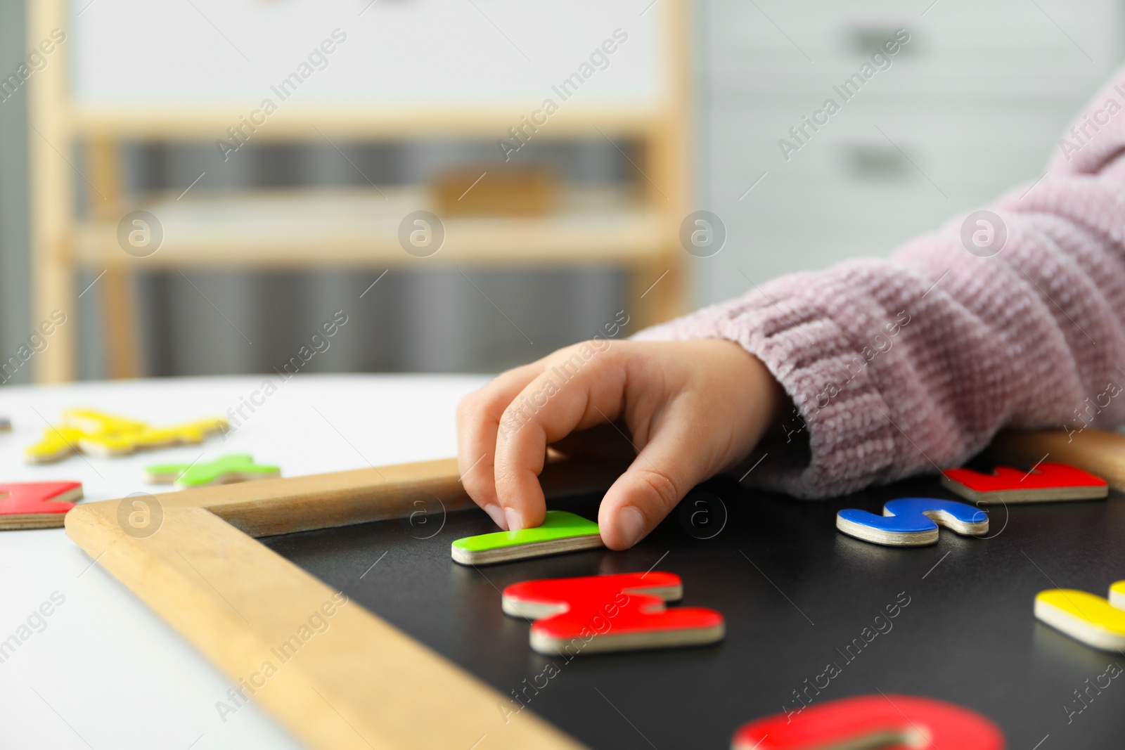 Photo of Little girl learning alphabet with magnetic letters at white table indoors, closeup