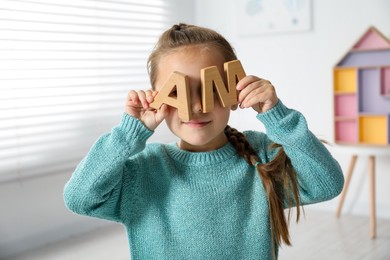 Photo of Little girl learning alphabet with wooden letters indoors