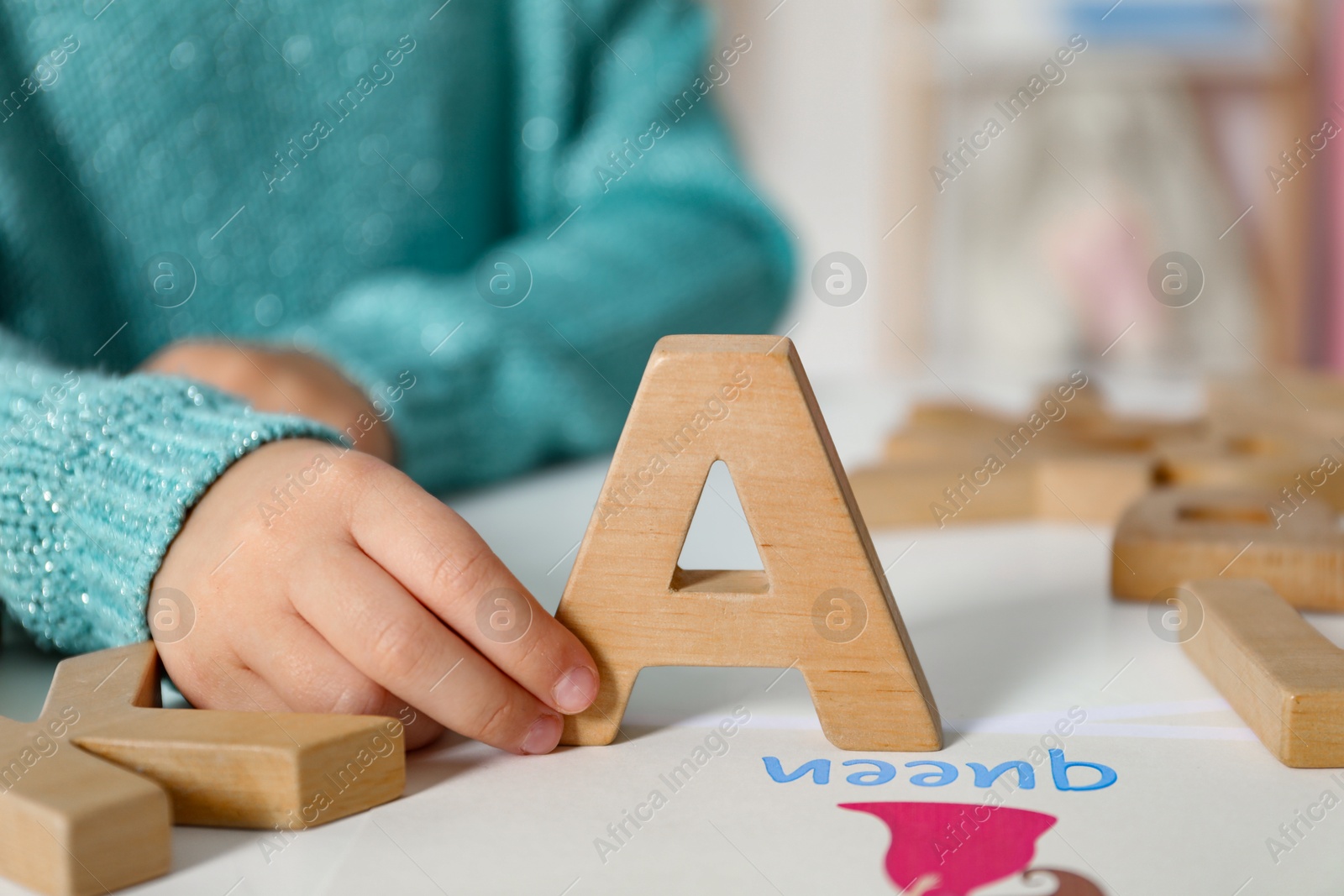 Photo of Little girl learning alphabet with wooden letters at white table indoors, closeup