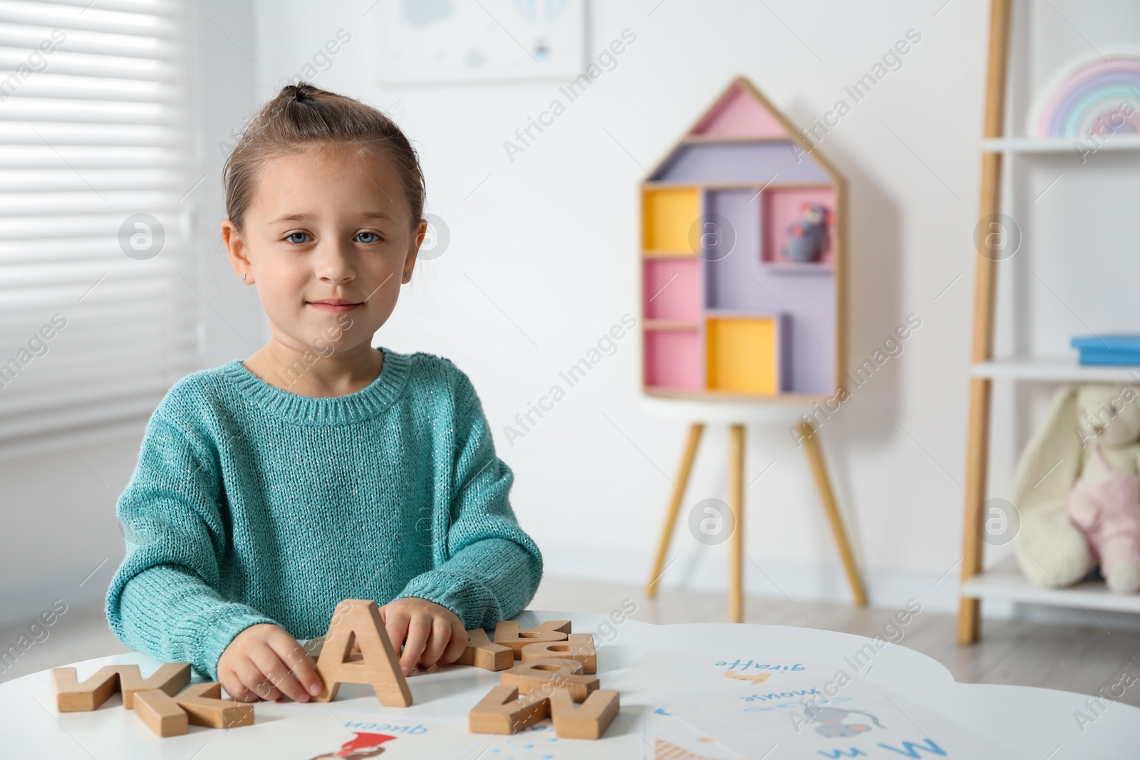 Photo of Little girl learning alphabet with wooden letters at white table indoors