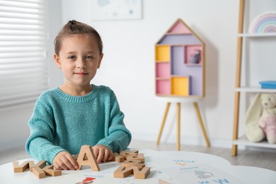 Photo of Little girl learning alphabet with wooden letters at white table indoors