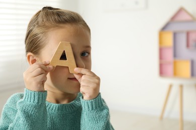 Photo of Learning alphabet. Little girl with wooden letter A indoors, space for text