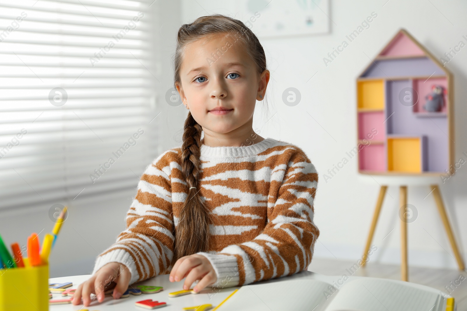 Photo of Little girl learning alphabet with magnetic letters at white table indoors