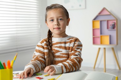 Photo of Little girl learning alphabet with magnetic letters at white table indoors