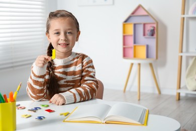 Photo of Little girl learning alphabet with magnetic letters at white table indoors