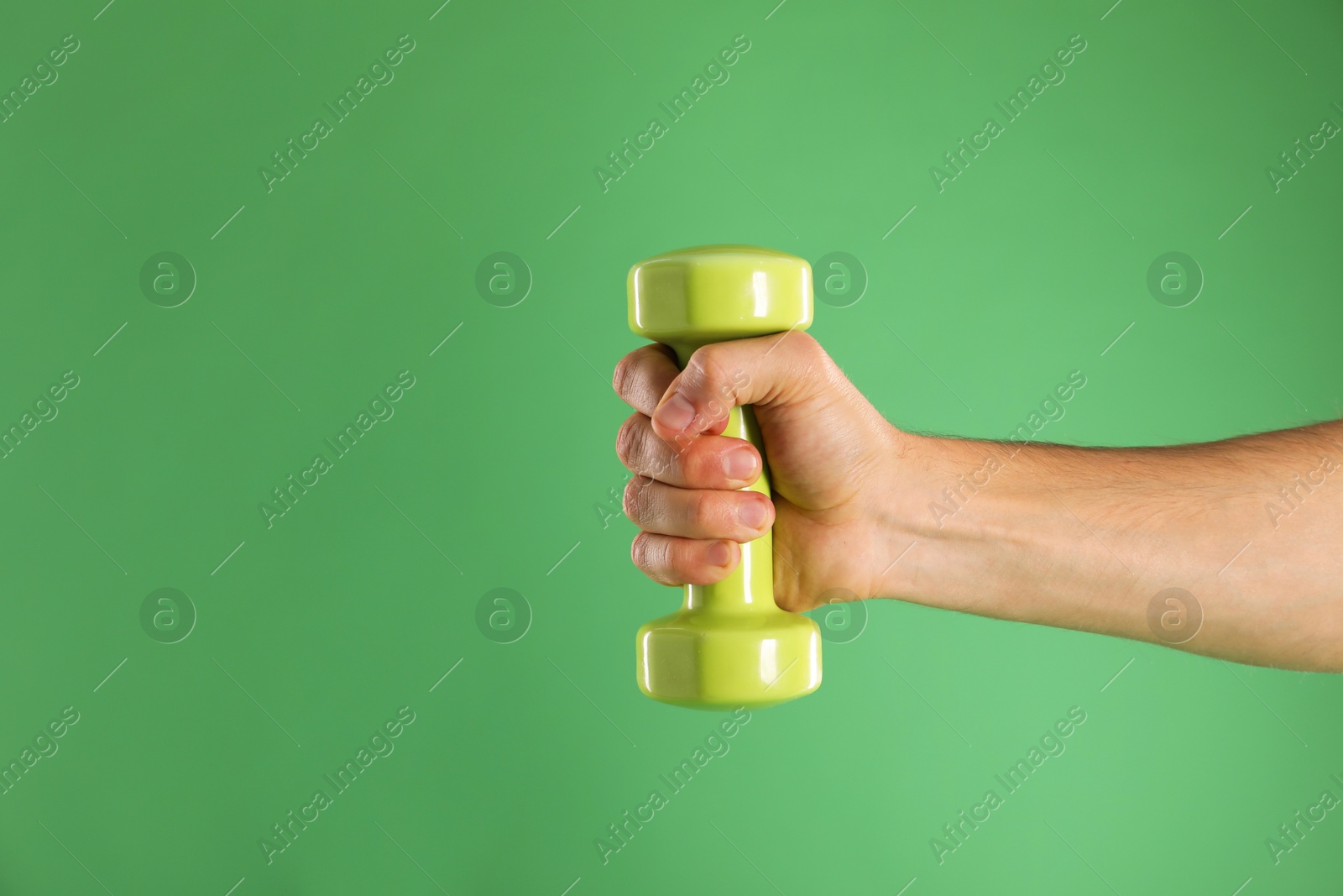 Photo of Man exercising with dumbbell on green background, closeup. Space for text