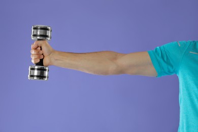 Photo of Man exercising with dumbbell on violet background, closeup