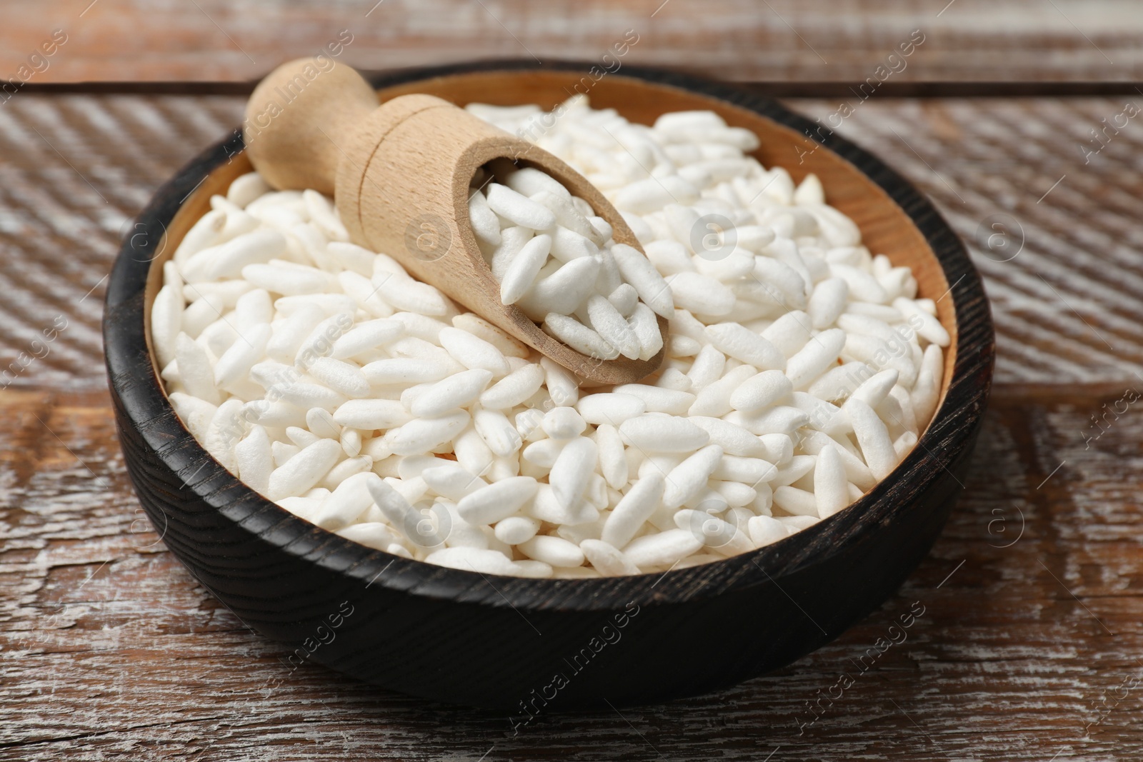 Photo of Puffed rice in bowl and scoop on wooden table, closeup