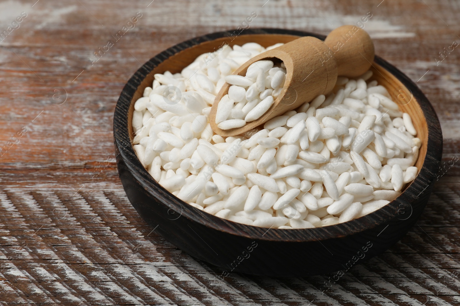 Photo of Puffed rice in bowl and scoop on wooden table, closeup