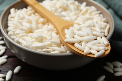 Photo of Puffed rice in bowl and spoon on wooden table, closeup