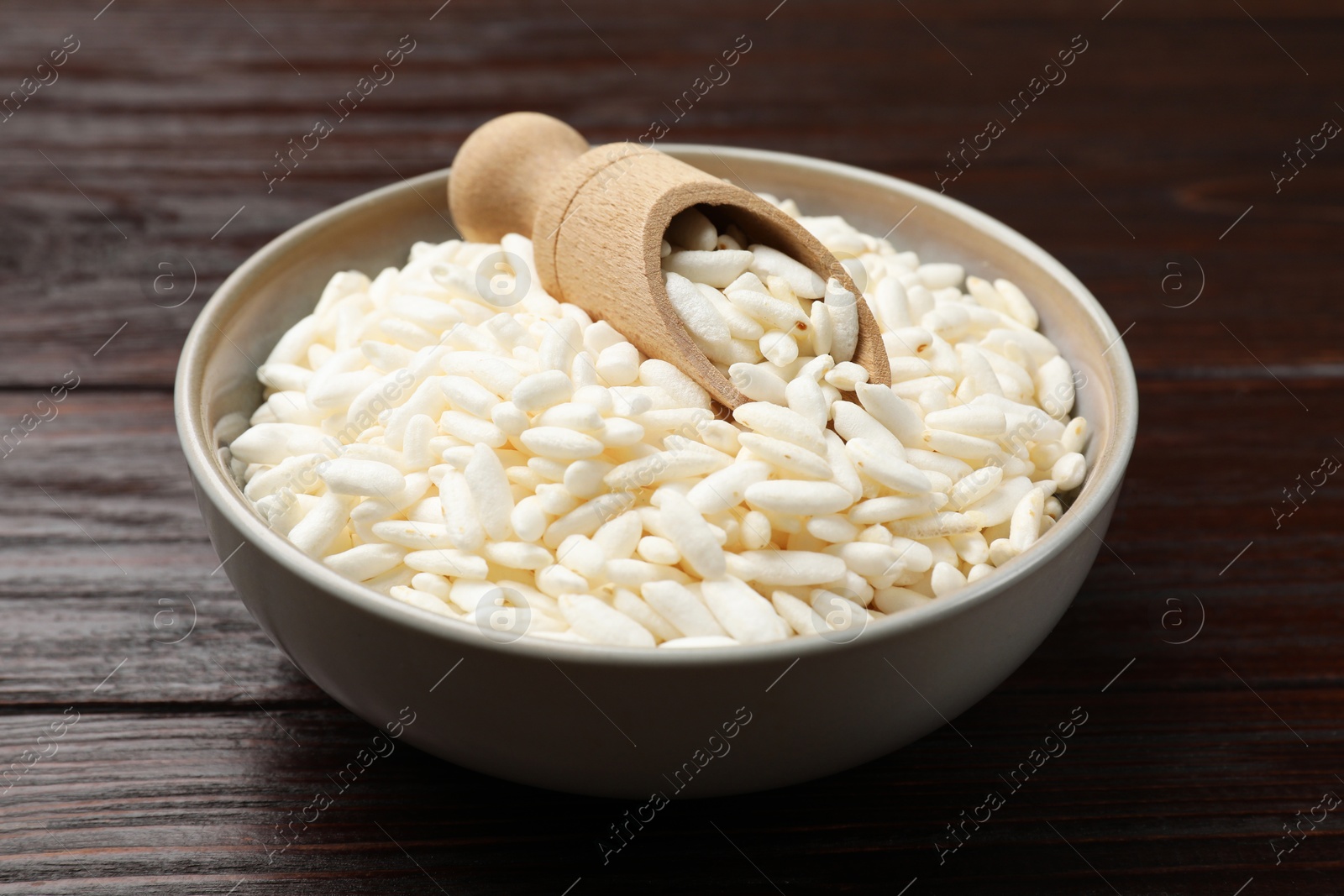 Photo of Puffed rice in bowl and scoop on wooden table, closeup