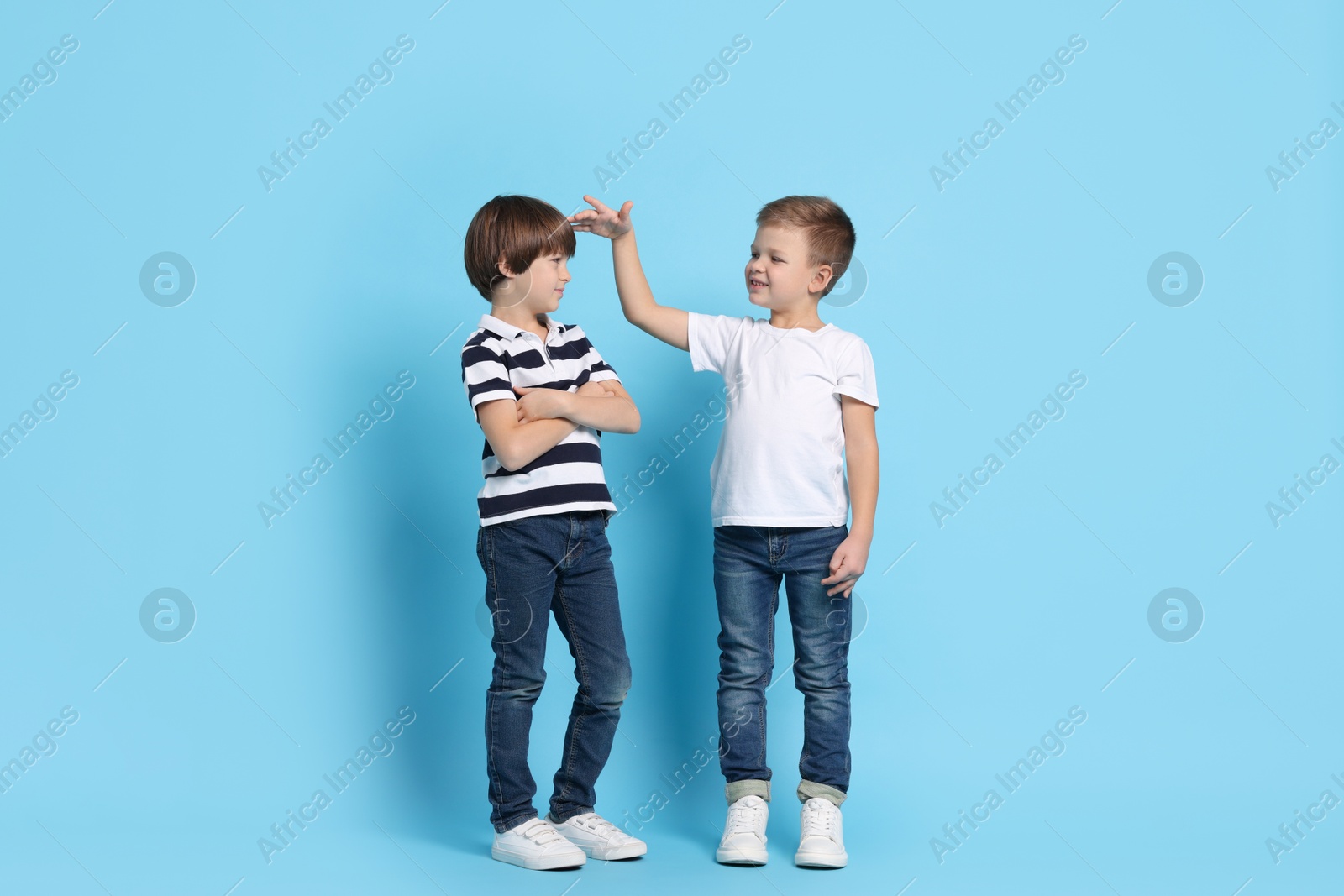 Photo of Cute brothers comparing their height on light blue background