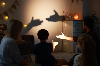 Photo of Shadow play. Father and his son making hand gestures like dogs on wall at home