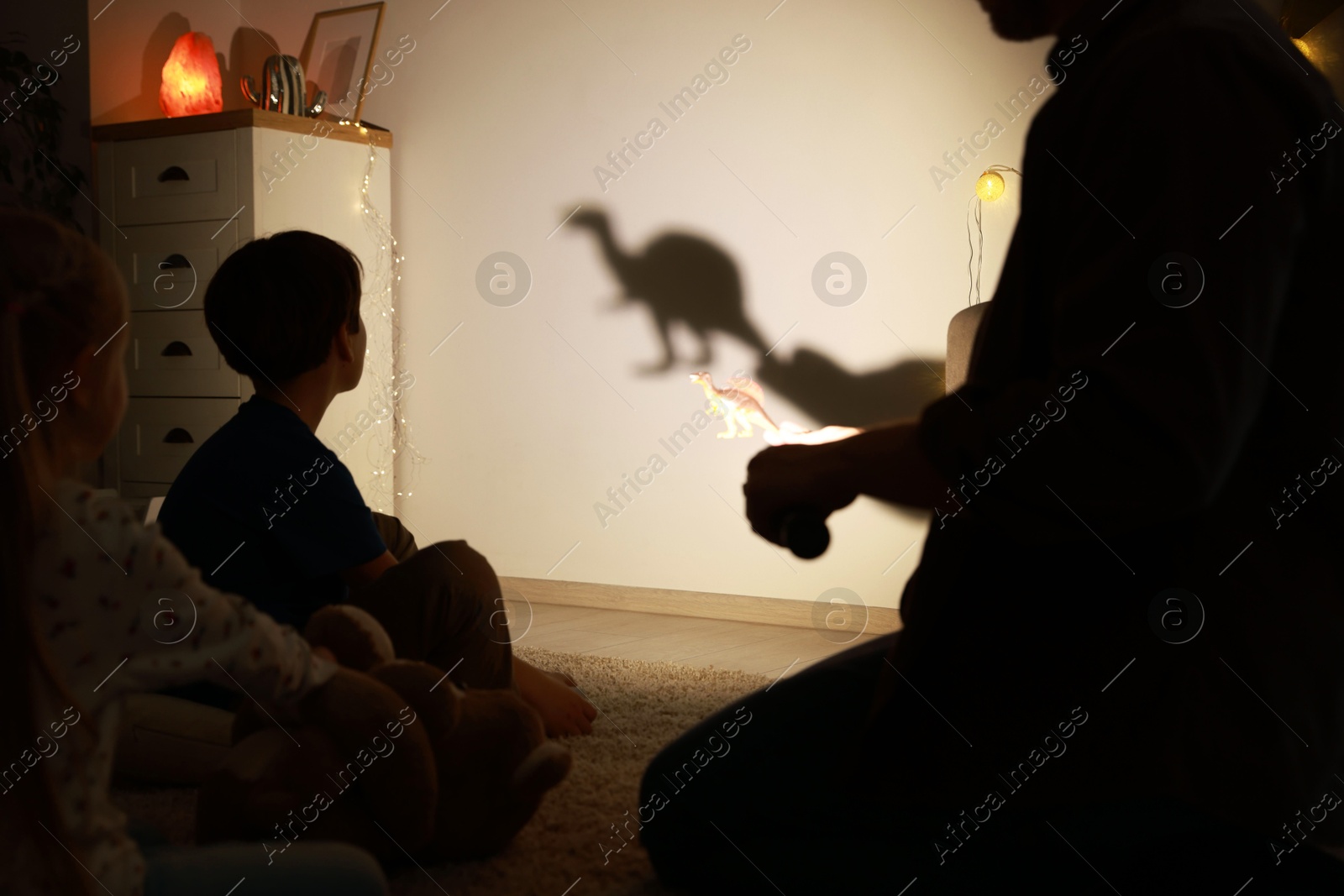 Photo of Father performing shadow play with toy dinosaur to his kids at home, closeup