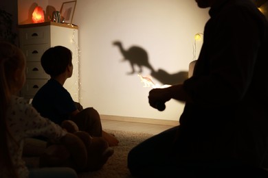 Photo of Father performing shadow play with toy dinosaur to his kids at home, closeup