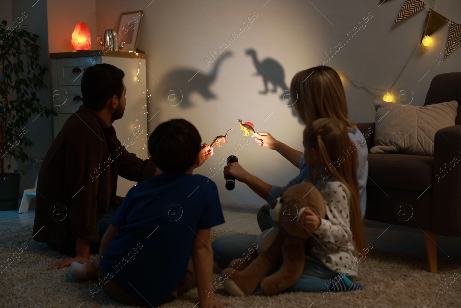 Photo of Parents performing shadow play with toy dinosaurs to their kids at home