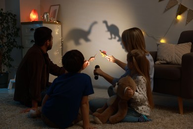 Photo of Parents performing shadow play with toy dinosaurs to their kids at home