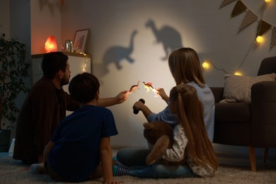 Photo of Parents performing shadow play with toy dinosaurs to their kids at home