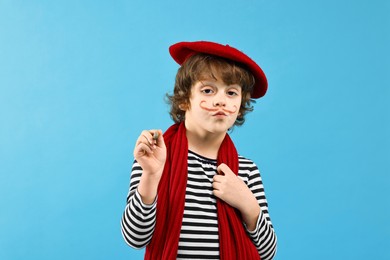 Photo of Cute boy in mime costume with brush on light blue background. Surprise party