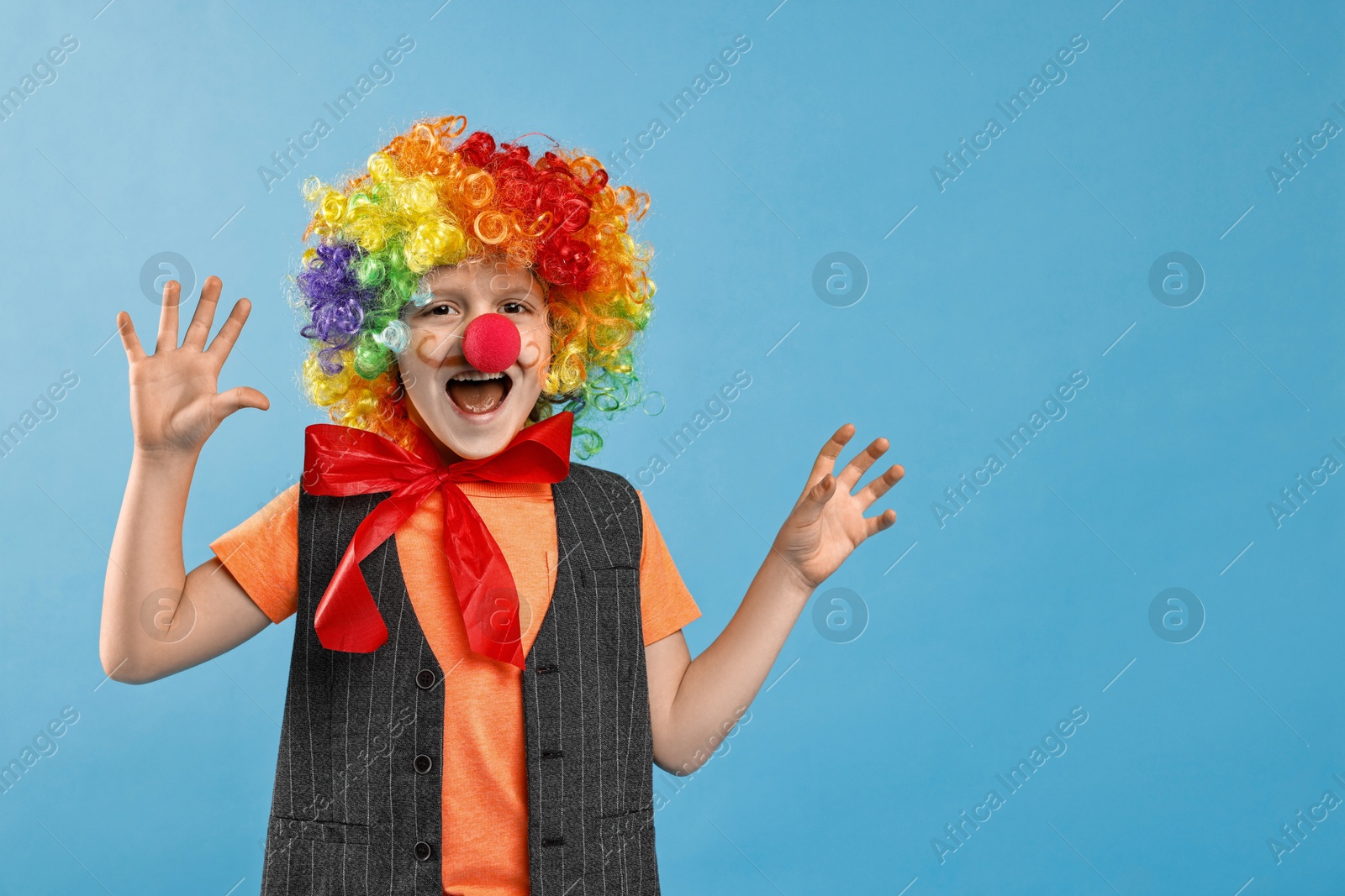 Photo of Little boy dressed like clown on light blue background, space for text. Surprise party