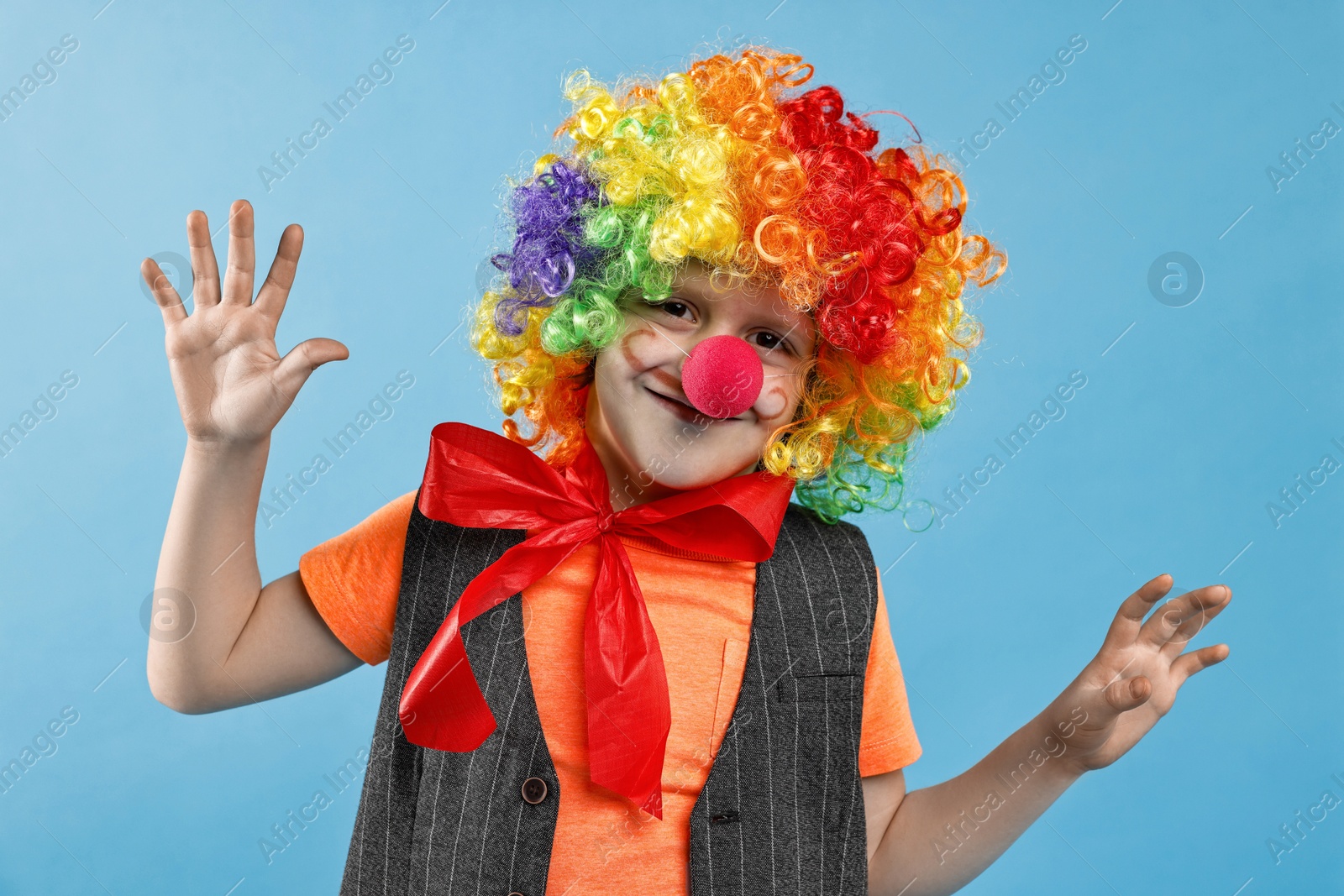 Photo of Happy boy dressed like clown on light blue background. Surprise party