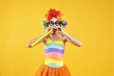 Photo of Girl dressed like clown with blowers on yellow background. Surprise party