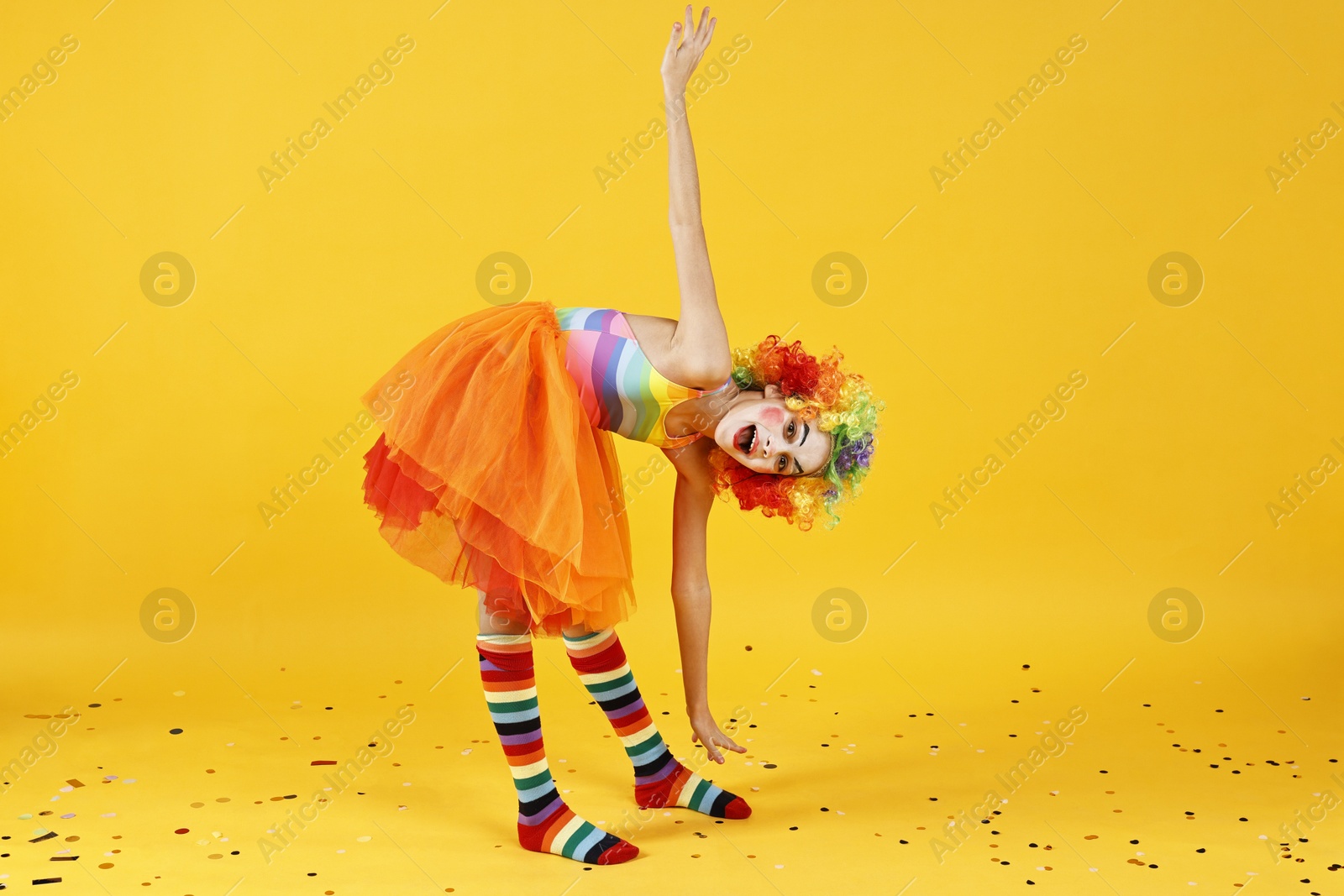 Photo of Cute girl dressed like clown and confetti on yellow background. Surprise party