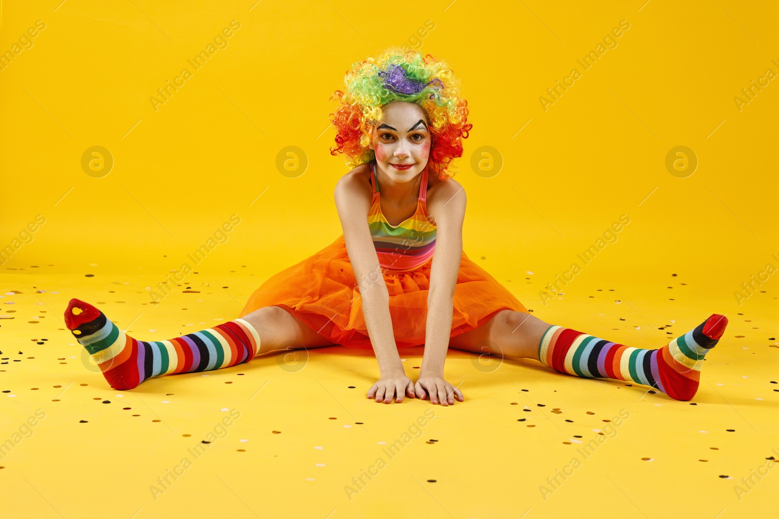 Photo of Cute girl dressed like clown and confetti on yellow background. Surprise party