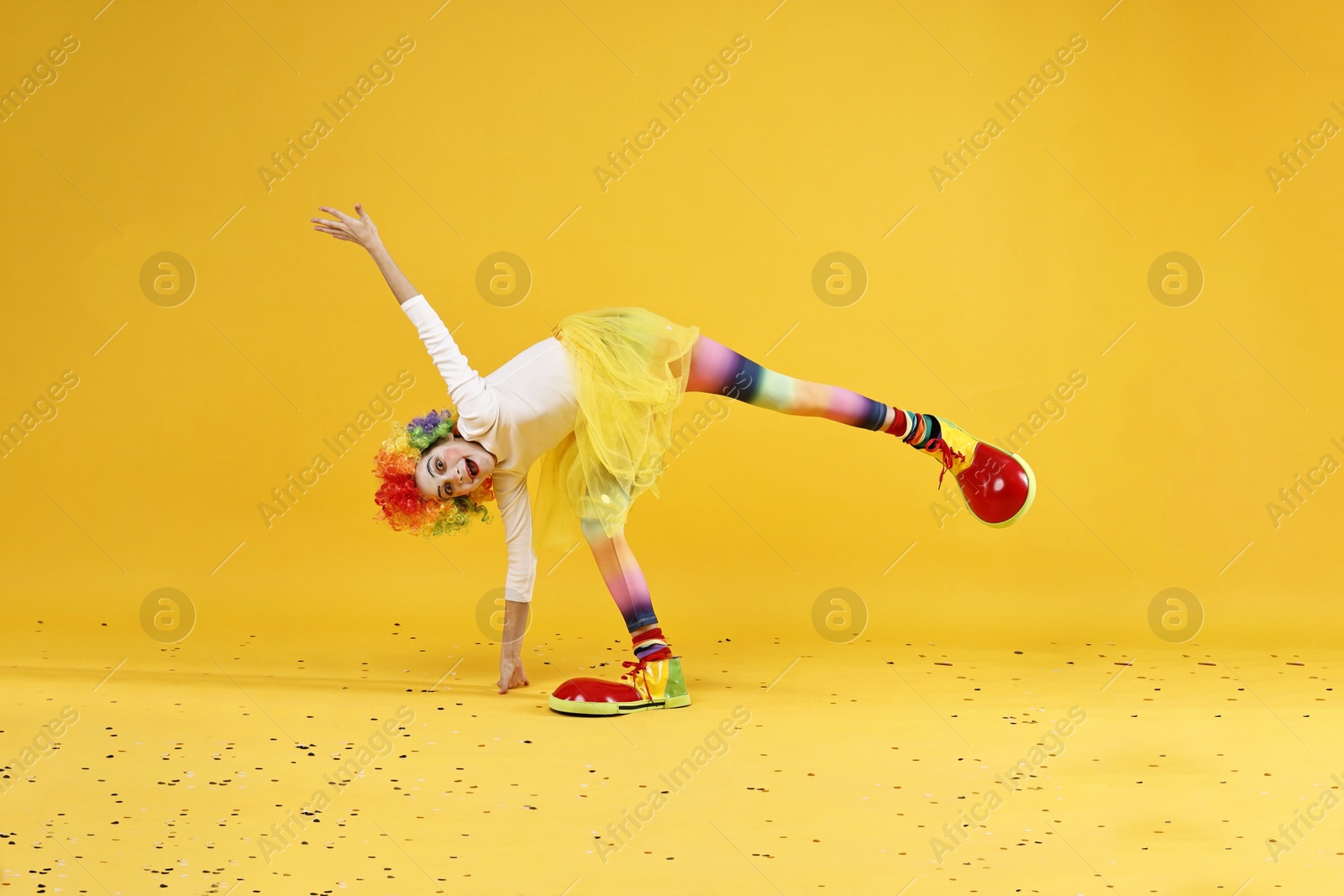 Photo of Cute girl dressed like clown having fun and confetti on yellow background. Surprise party