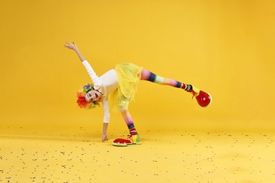 Photo of Cute girl dressed like clown having fun and confetti on yellow background. Surprise party