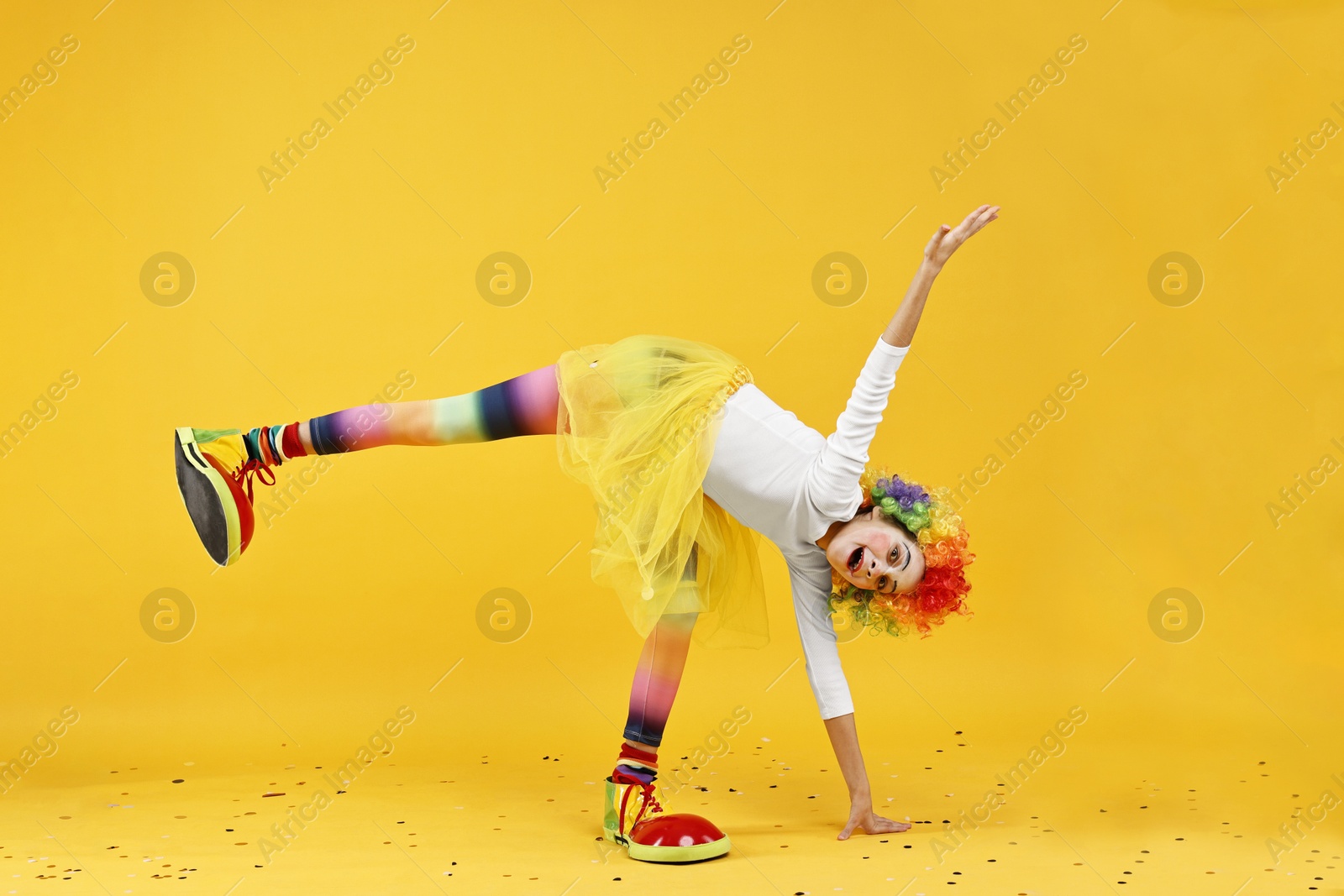 Photo of Cute girl dressed like clown having fun and confetti on yellow background. Surprise party