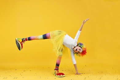 Photo of Cute girl dressed like clown having fun and confetti on yellow background. Surprise party