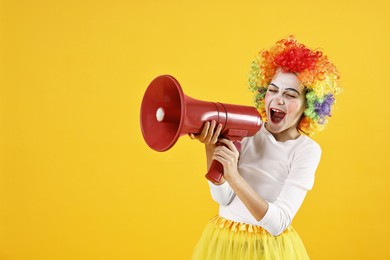 Photo of Cute girl dressed like clown shouting in megaphone on yellow background, space for text. Surprise party