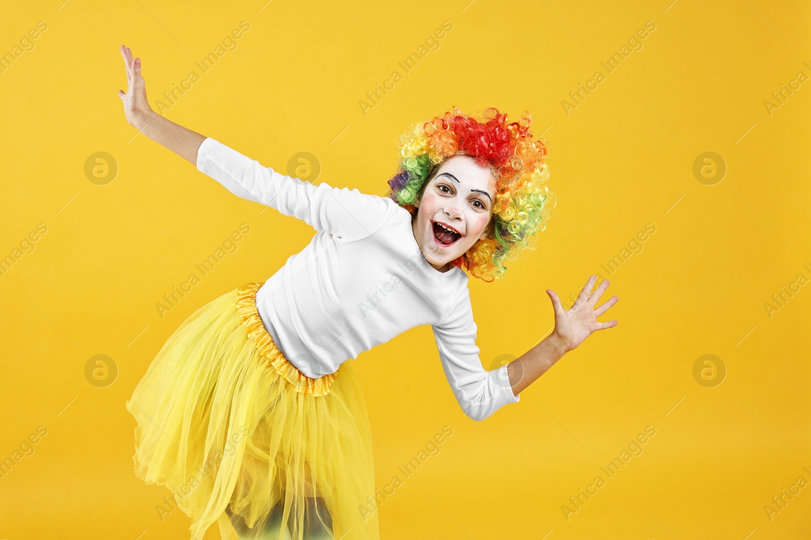 Photo of Happy girl dressed like clown on yellow background. Surprise party