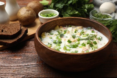 Photo of Delicious okroshka soup with kefir and bread on wooden table, closeup