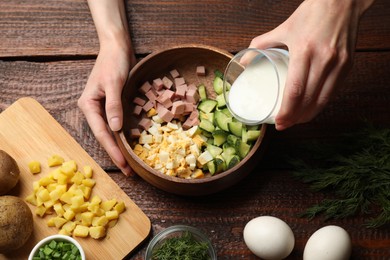 Photo of Woman making okroshka soup with kefir at wooden table, top view