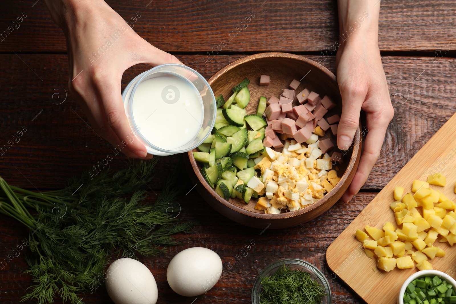 Photo of Woman making okroshka soup with kefir at wooden table, top view