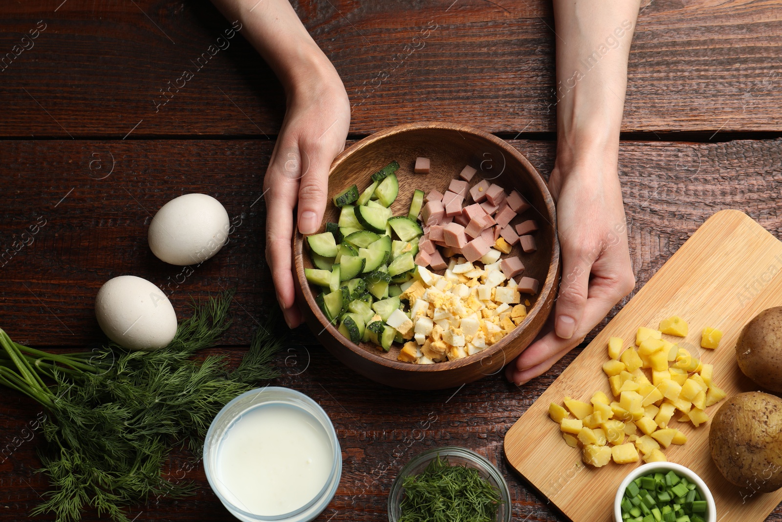 Photo of Woman making okroshka soup at wooden table, top view