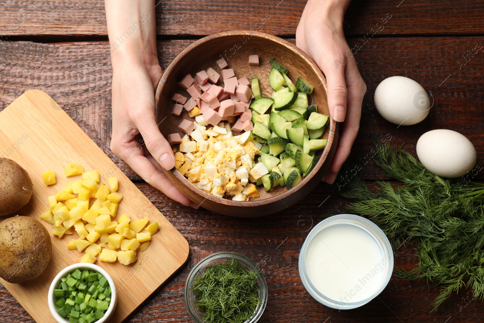 Photo of Woman making okroshka soup at wooden table, top view