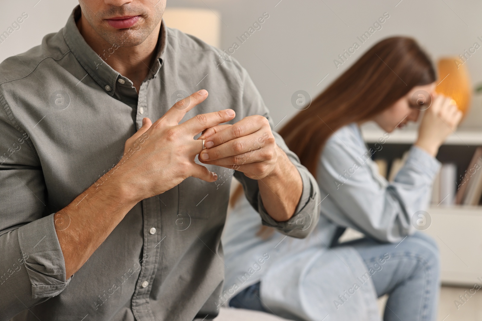 Photo of Man taking off engagement ring after quarrel with his wife at home, closeup