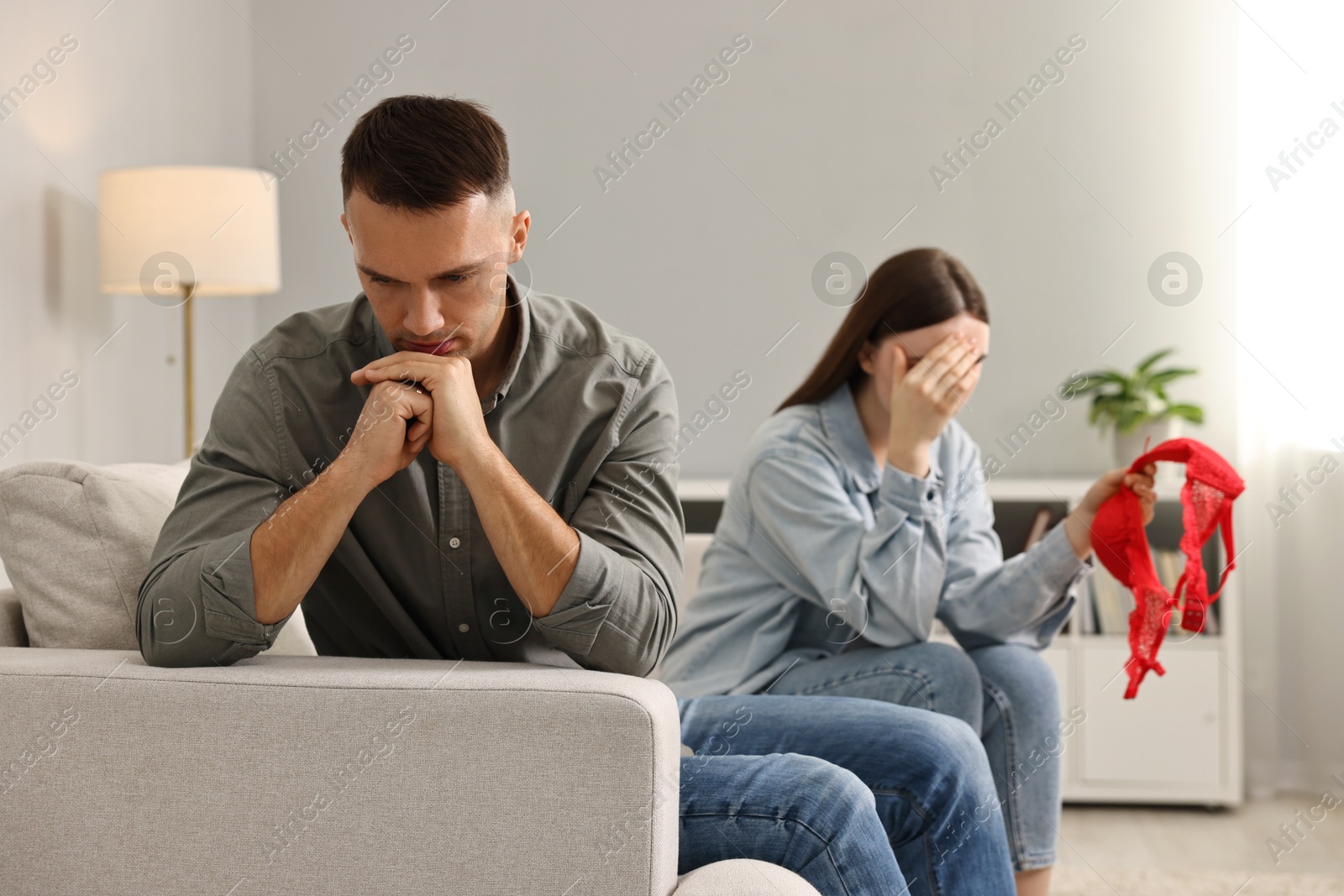 Photo of Stressed wife with mistress bra as proof and her unfaithful husband ignoring each other at home, selective focus