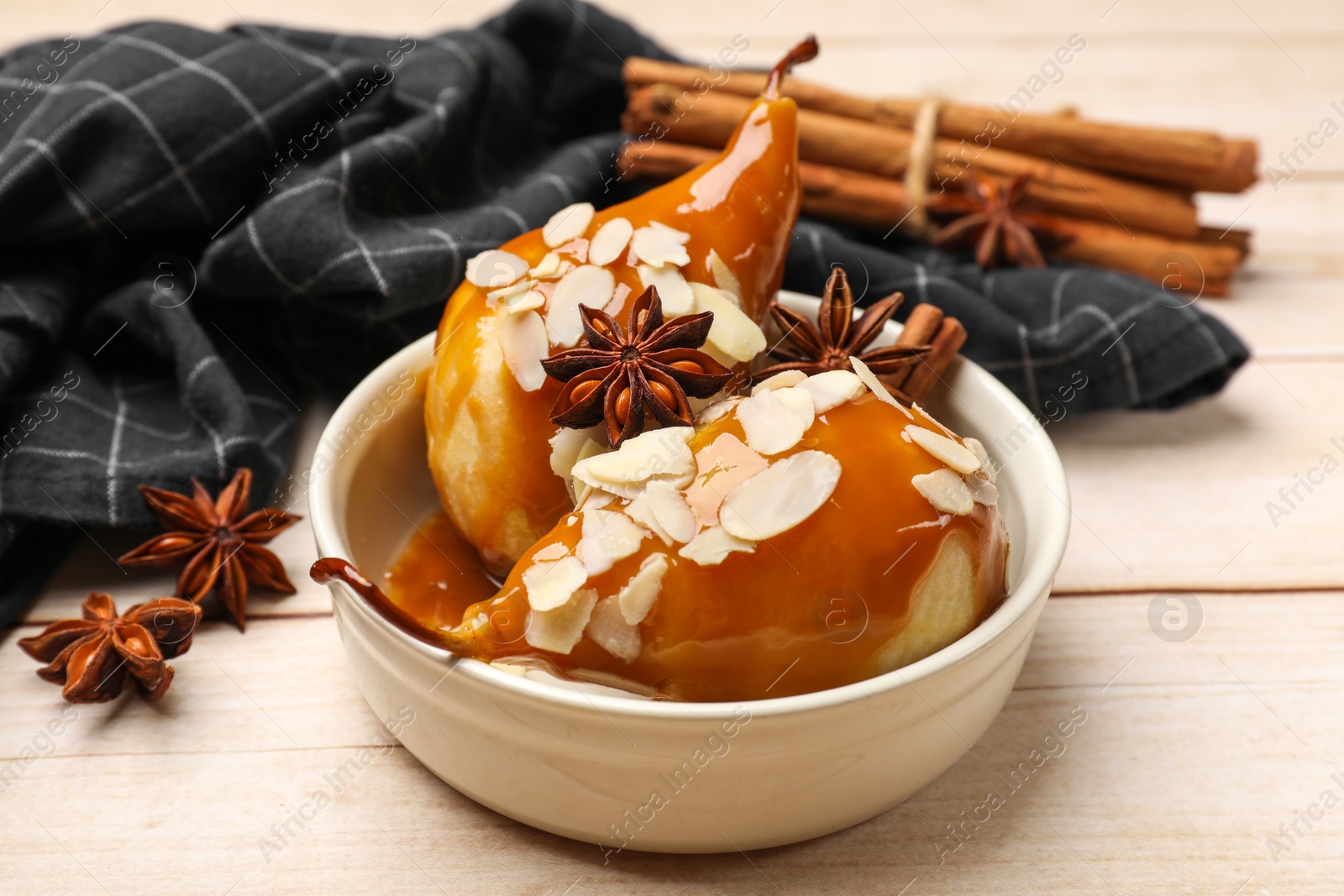 Photo of Delicious pears with caramel sauce, almond flakes and spices on white wooden table, closeup