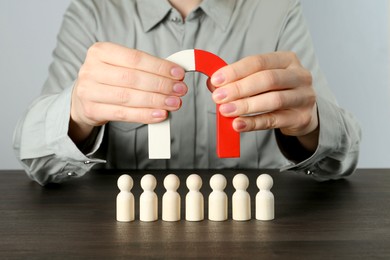 Photo of Woman with magnet attracting human figures at wooden table, closeup