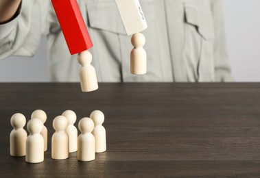 Photo of Attracting human figures with magnet at wooden table, closeup