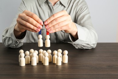 Photo of Woman with magnet attracting human figures at wooden table, closeup