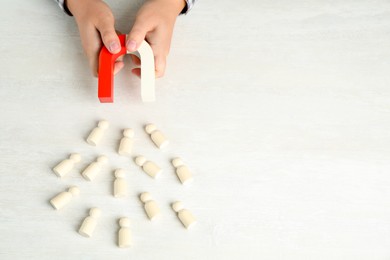 Photo of Man with magnet attracting wooden human figures at light table, above view. Space for text