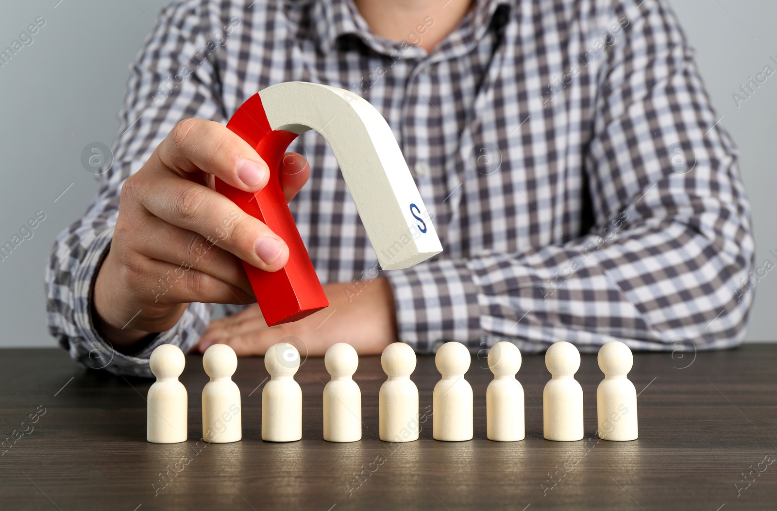 Photo of Man with magnet attracting human figures at wooden table, closeup