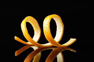 Photo of One fresh orange peel on black mirror surface, closeup