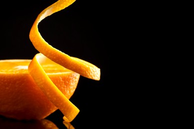 Photo of Fresh orange peel and half of fruit on black mirror surface, closeup. Space for text