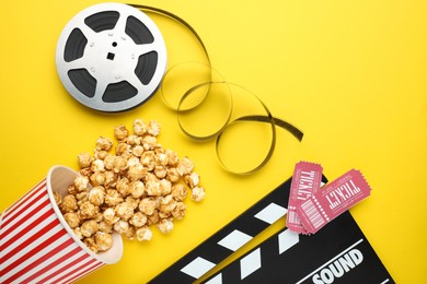 Photo of Movie clapper, sweet popcorn, tickets and film reel on yellow background, flat lay